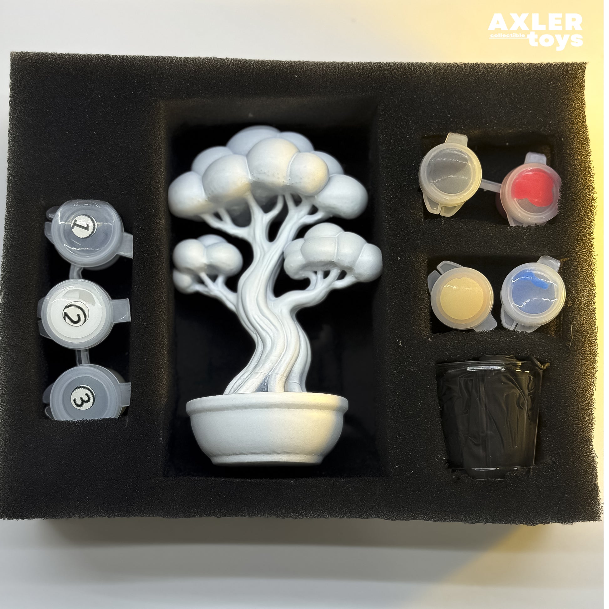 Model kit of a bonsai tree with paint pots in a foam tray, brand 'Axler Toys' visible.