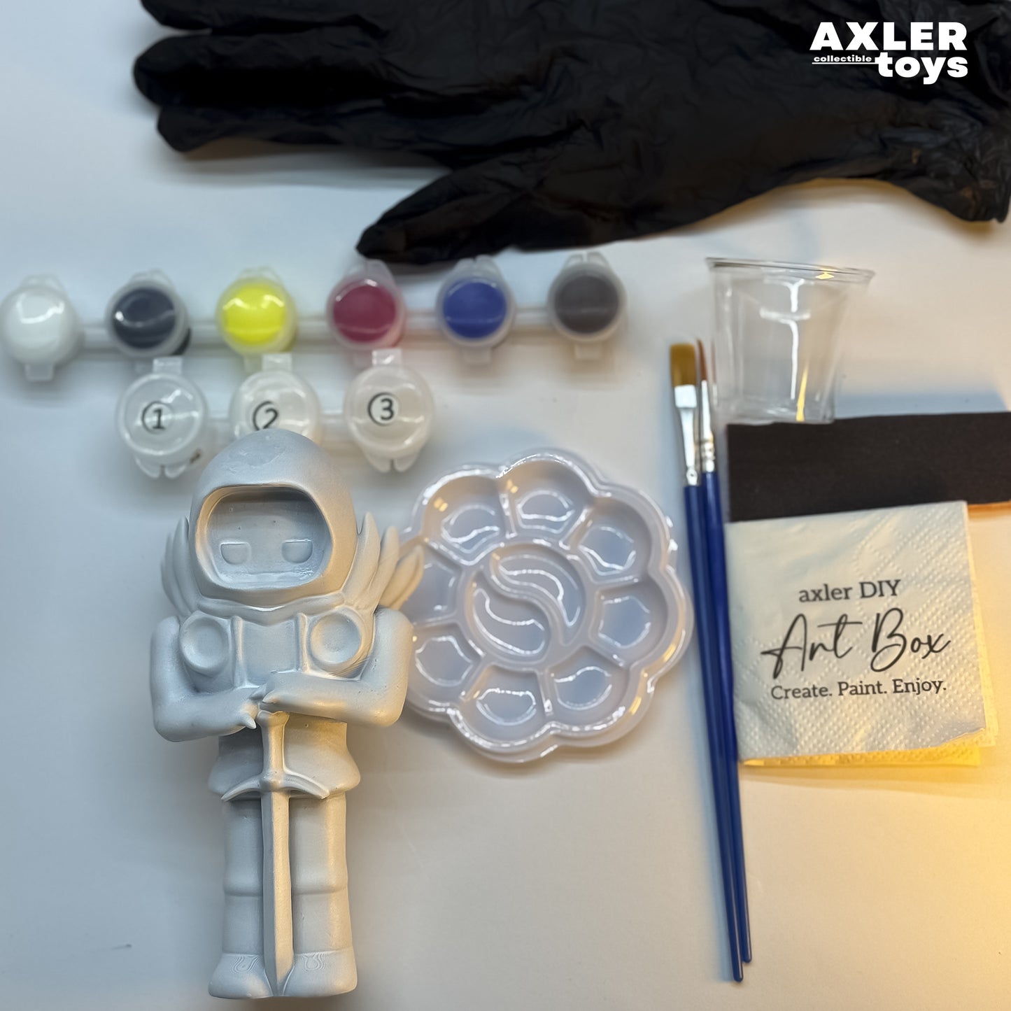 Axler Toys art supplies including paint, brushes, and a mold on a white surface.